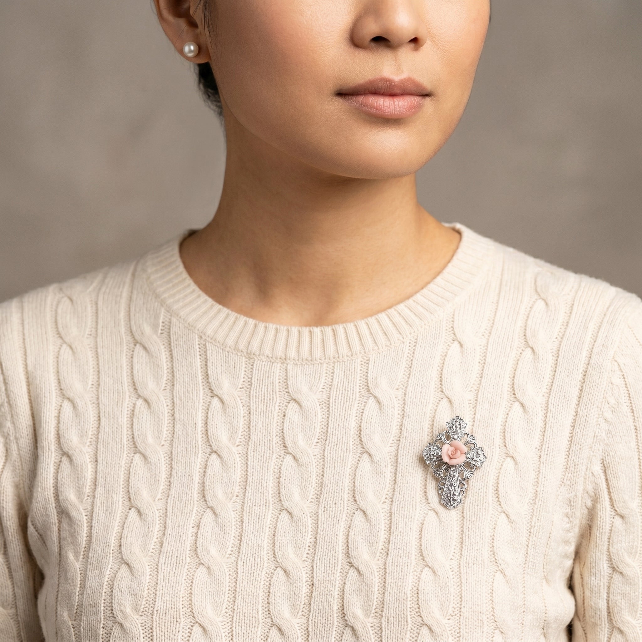 Woman in a cream sweater wearing a silver tone cross brooch with a genuine handmade porcelain rose center