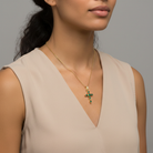 Woman wearing a gold necklace with a green cross pendant against a neutral background
