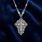 Silver necklace with a detailed cross crucifix pendant on a dark blue fabric background