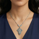 Close-up of a woman wearing a silver necklace with a detailed INRI cross crucifix pendant on a dark background