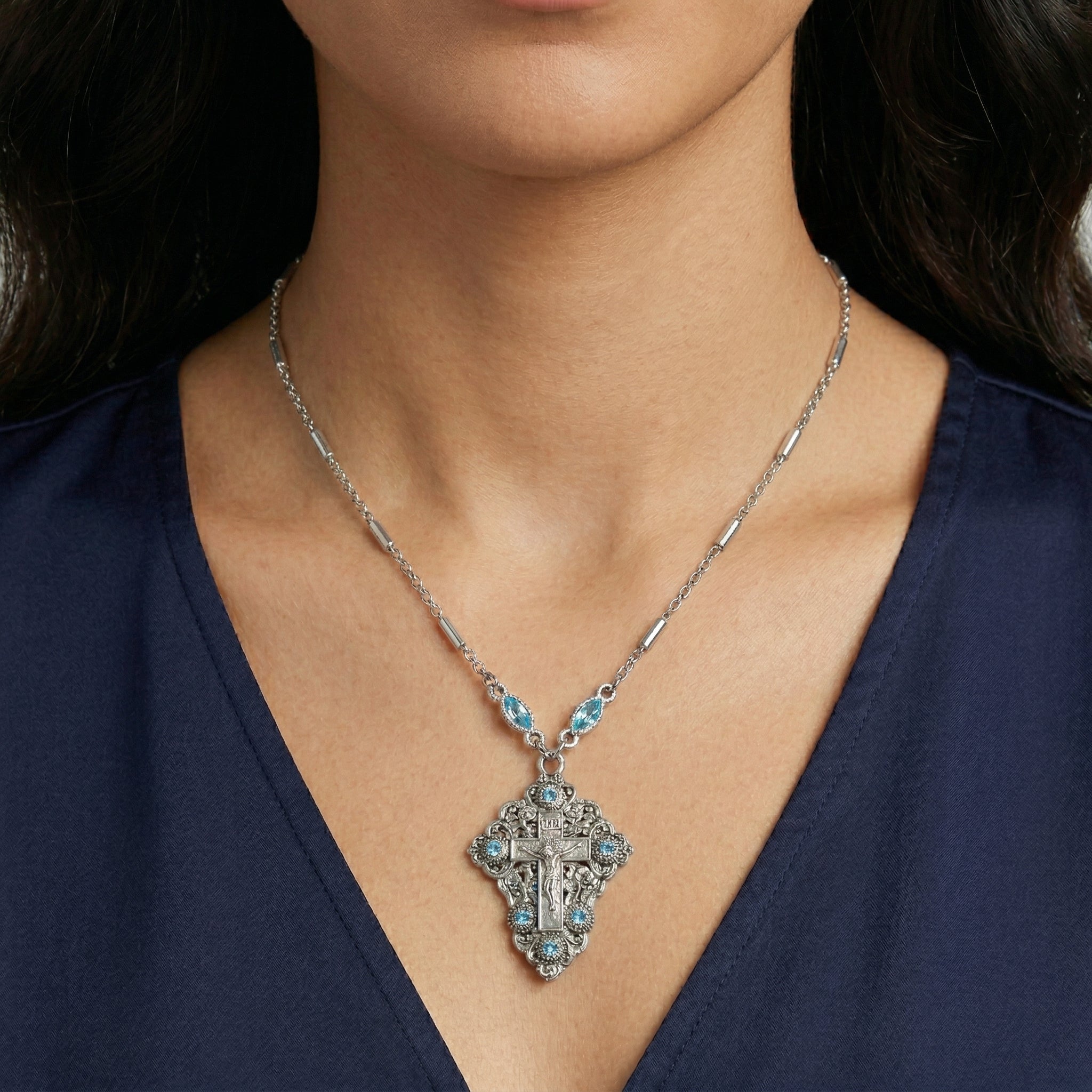 Close-up of a woman wearing a silver necklace with a detailed INRI cross crucifix pendant on a dark background
