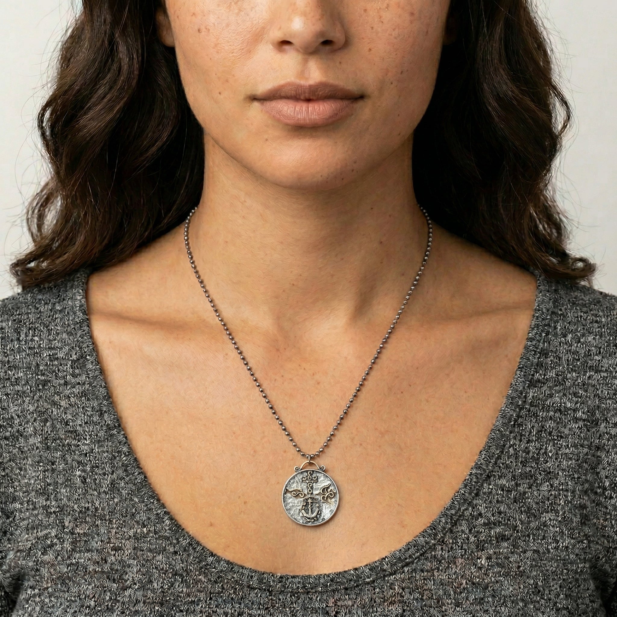 Person wearing a necklace with a religious cross dove and anchor pendant against a neutral background