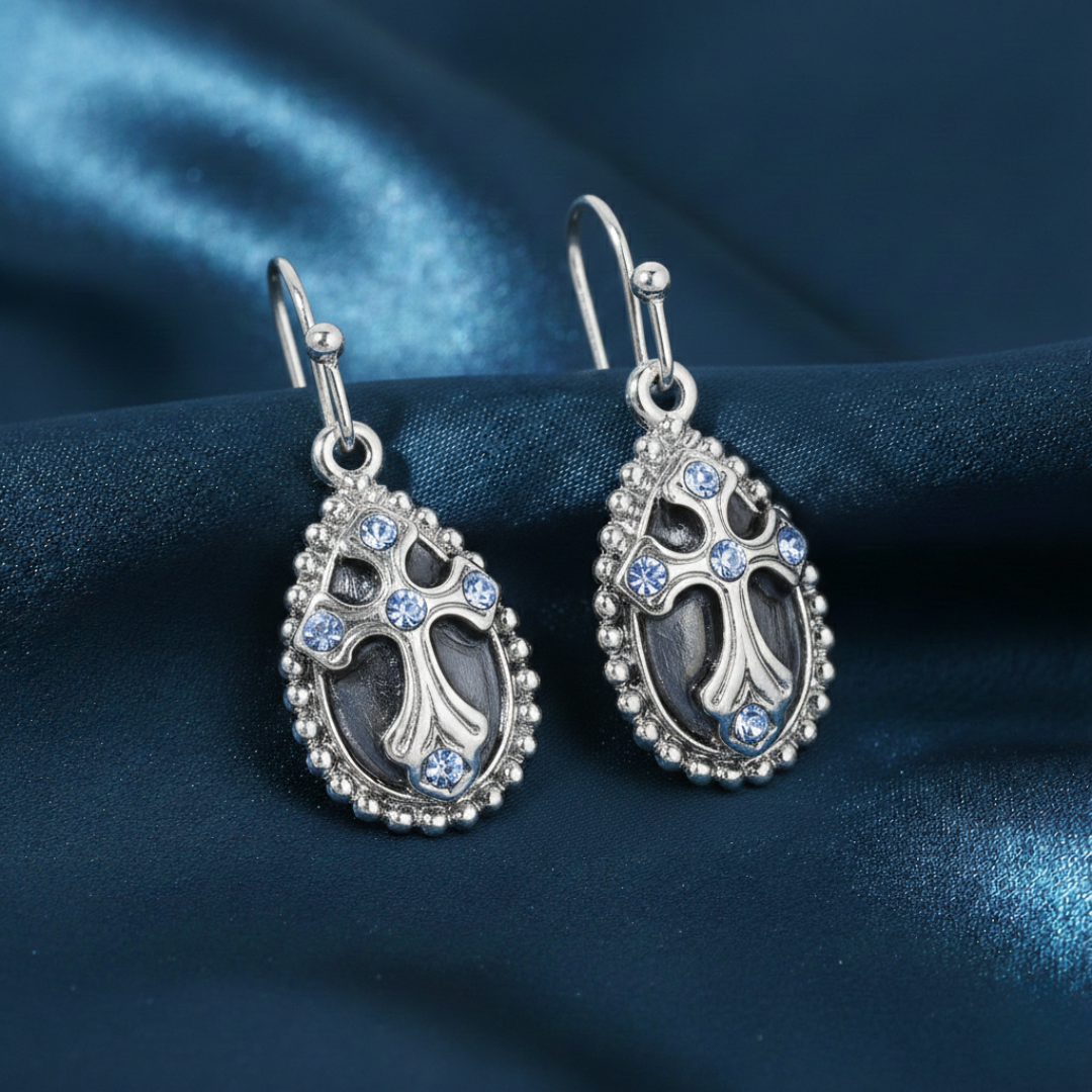 Silver earrings with blue gemstones and a cross on a blue fabric background