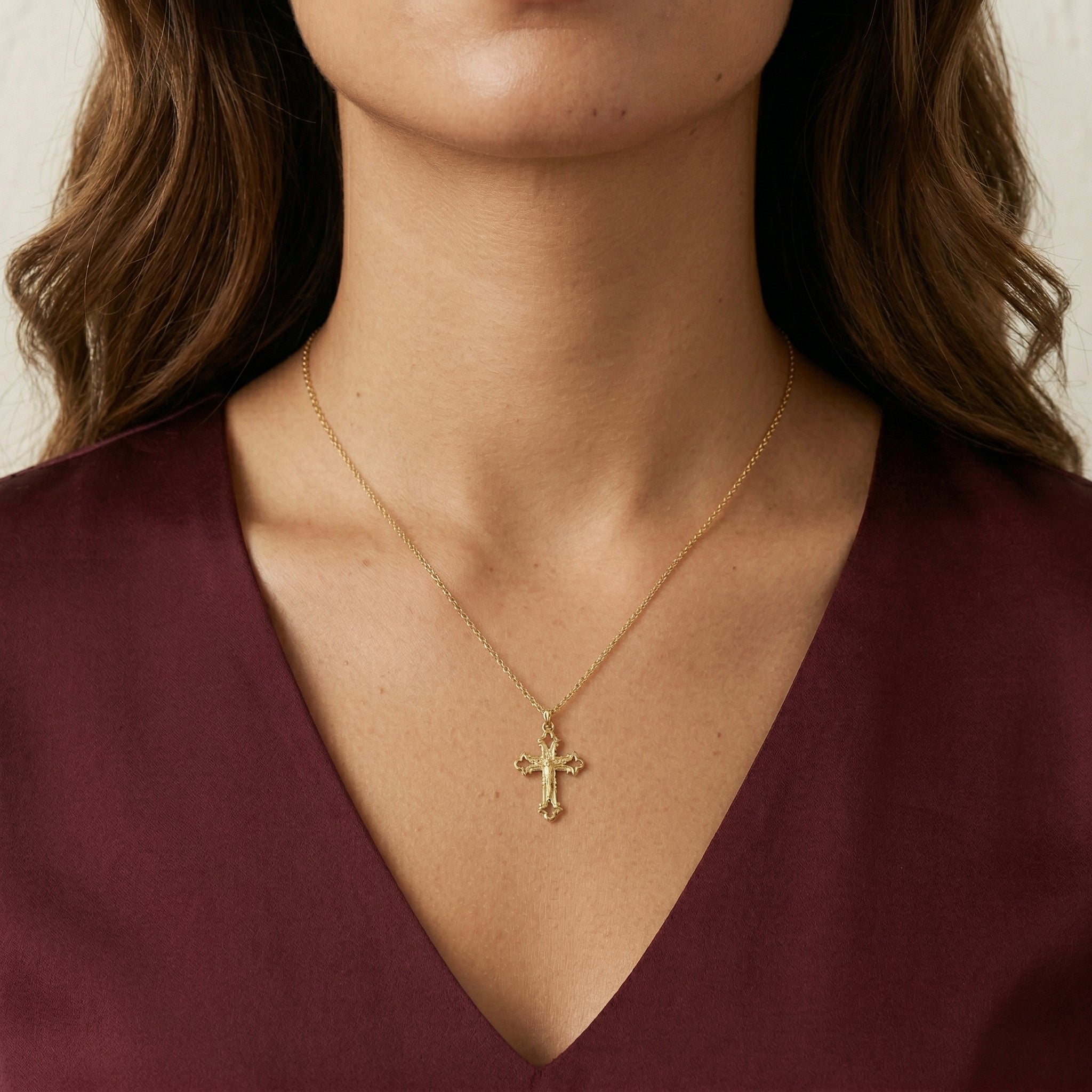 Gold necklace with a crucifix pendant worn by a person in a burgundy top.