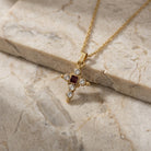 Gold necklace with a cross pendant that has both clear and red crystal accents on a marble surface