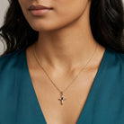 Woman wearing a gold necklace with a cross pendant that has clear crystal accents and a red crystal in the middle