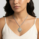 Woman wearing a silver tone necklace with crystals on the chain and an Our Lady of Guadalupe pendant against a neutral background