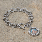 Mother Mary and Child silver tone toggle chain bracelet with clear crystal accents resting on a granite stone surface