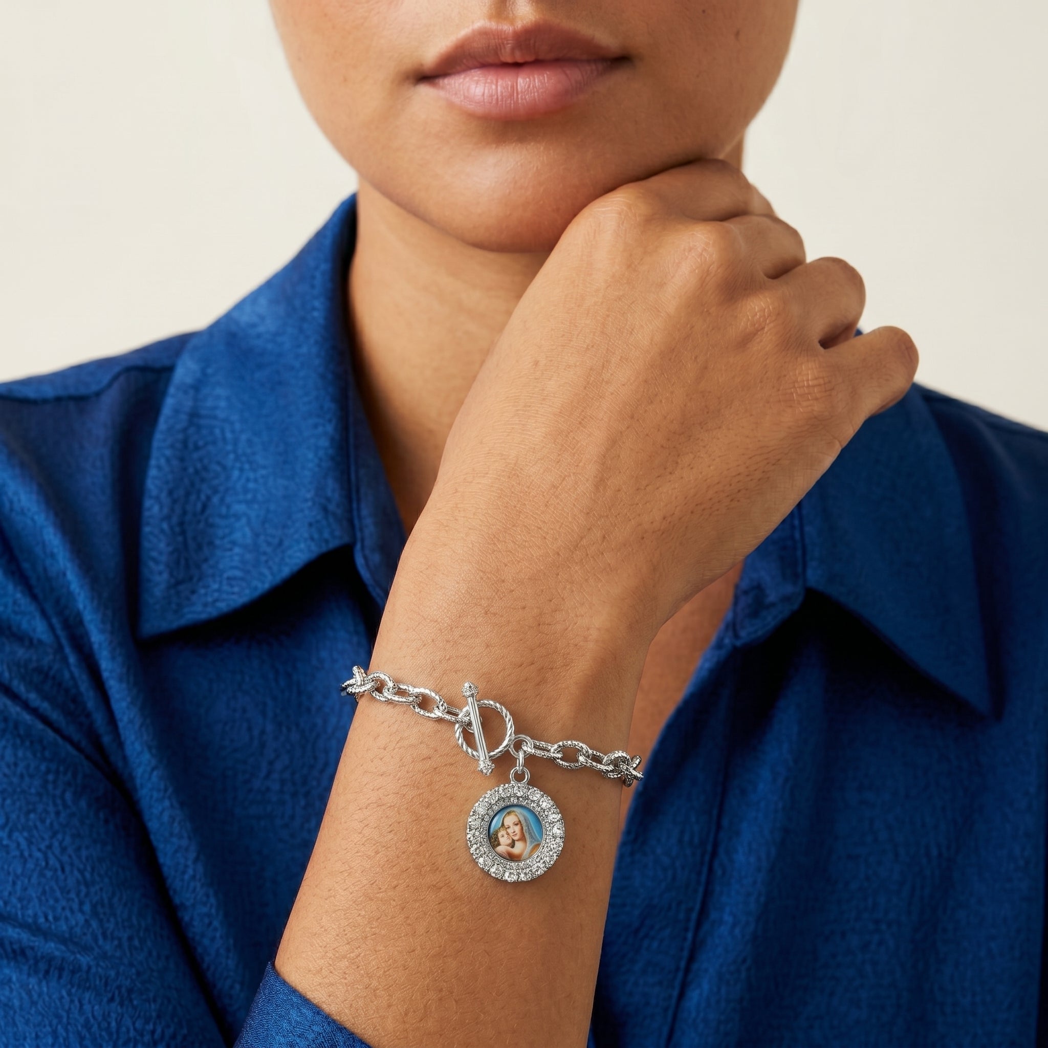 Woman in a blue shirt wearing a silver tone Mother Mary and Child toggle chain bracelet. 