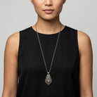 Woman wearing a black sleeveless top with a silver locket necklace against a gray background