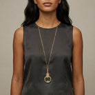 Woman wearing a long gold necklace with a magnifying glass pendant and Mother Mary and Child decal against a neutral background