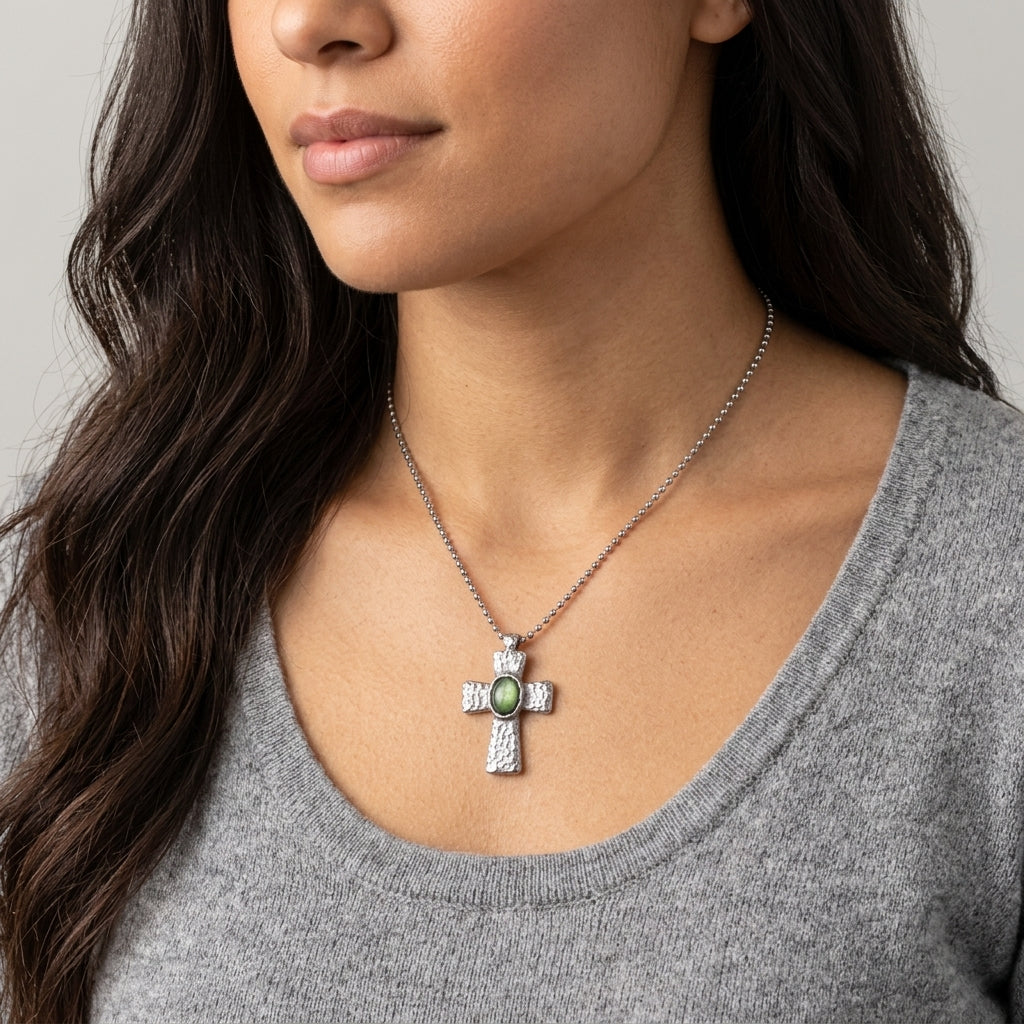 Woman wearing a silver cross necklace with a green gemstone on a gray background