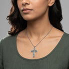 Woman wearing a silver necklace with a cross pendant on a gray background