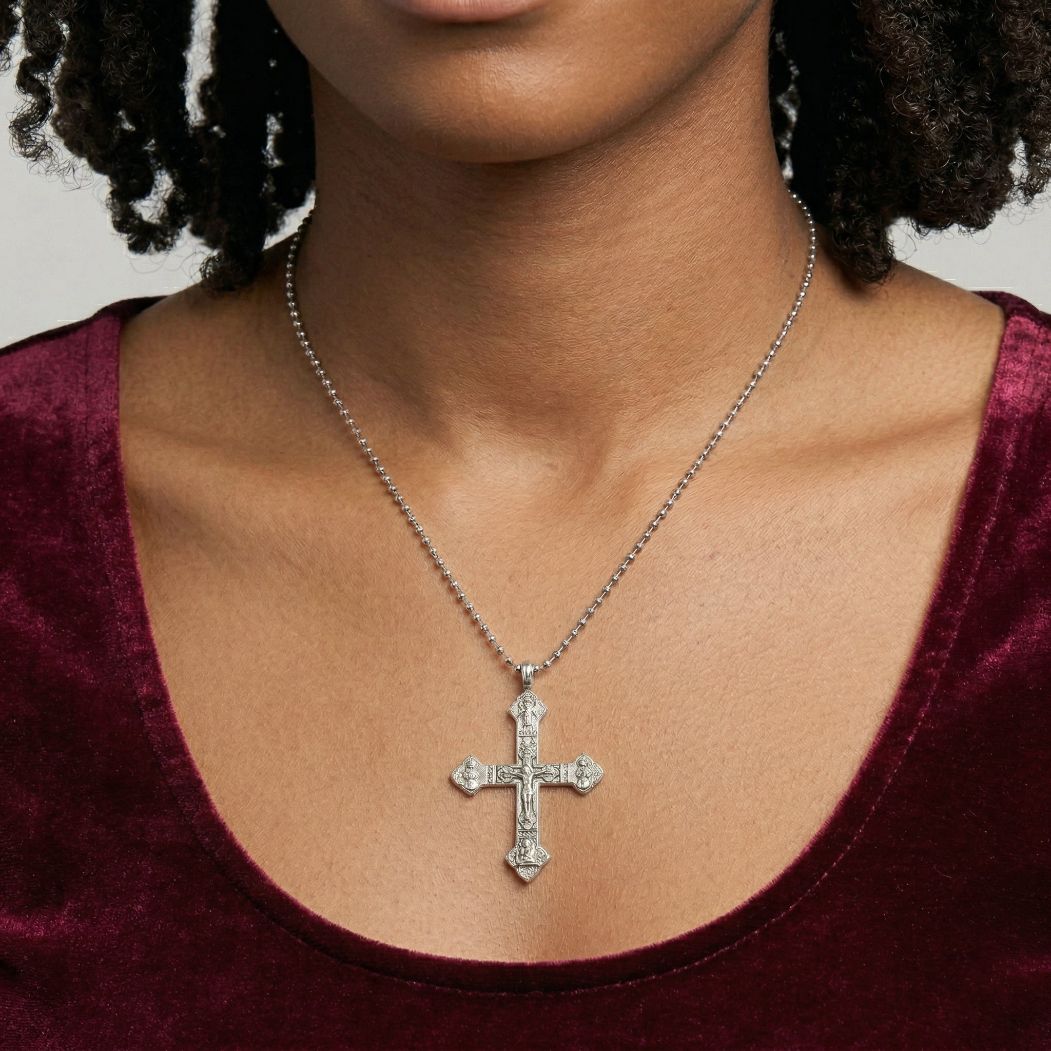 Person wearing a silver crucifix necklace with a maroon top