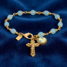 Gold bracelet with blue beads and a crucifix charm on a blue background