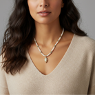 Woman wearing a pearl necklace with a religious pendant on a gray background