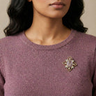 Close-up of a person wearing a purple sweater with a decorative Mother Mary and Child amethyst brooch.