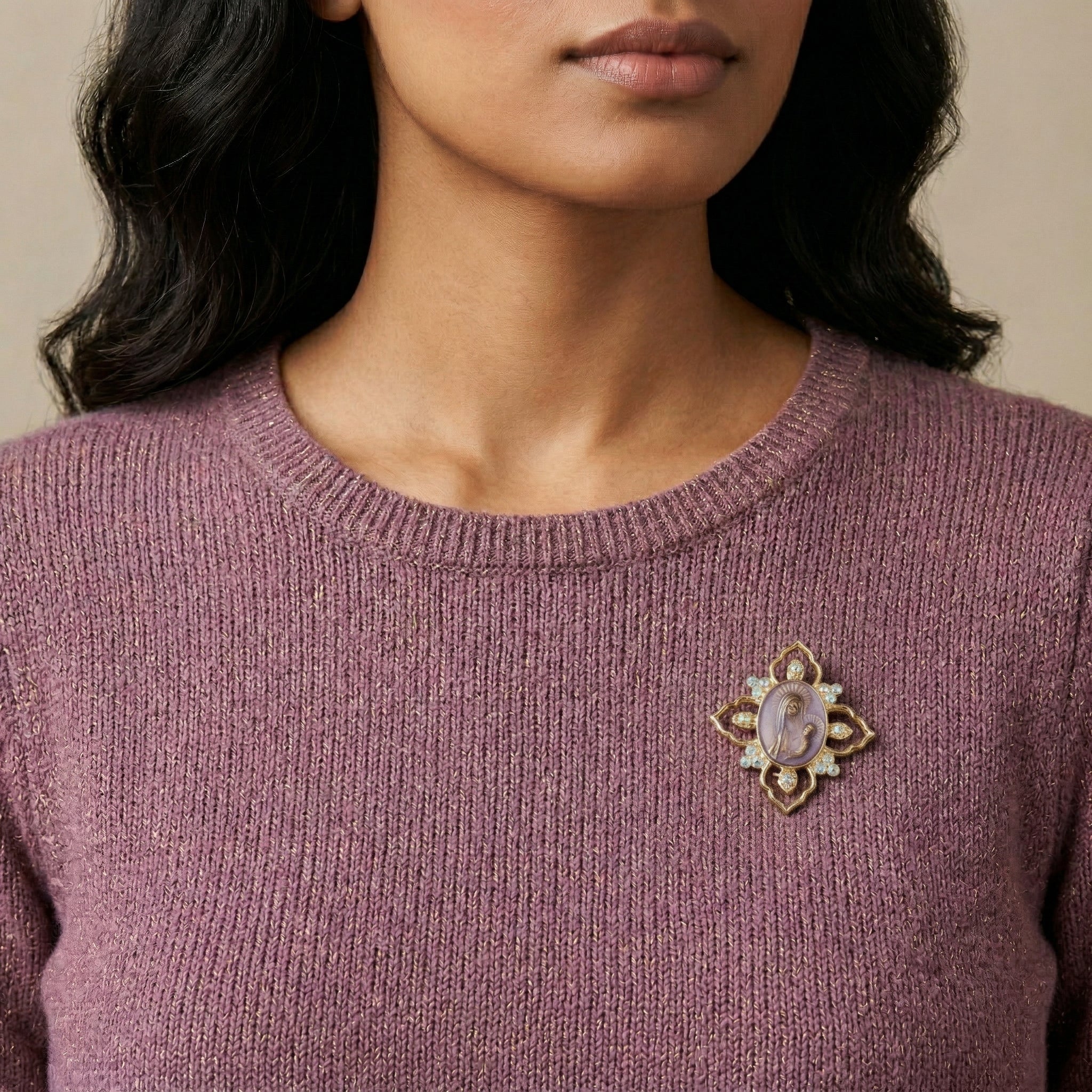 Close-up of a person wearing a purple sweater with a decorative Mother Mary and Child amethyst brooch.