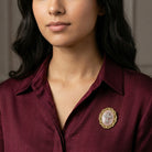 Close-up of a woman wearing a burgundy shirt with a decorative gold tone rose quartz brooch.