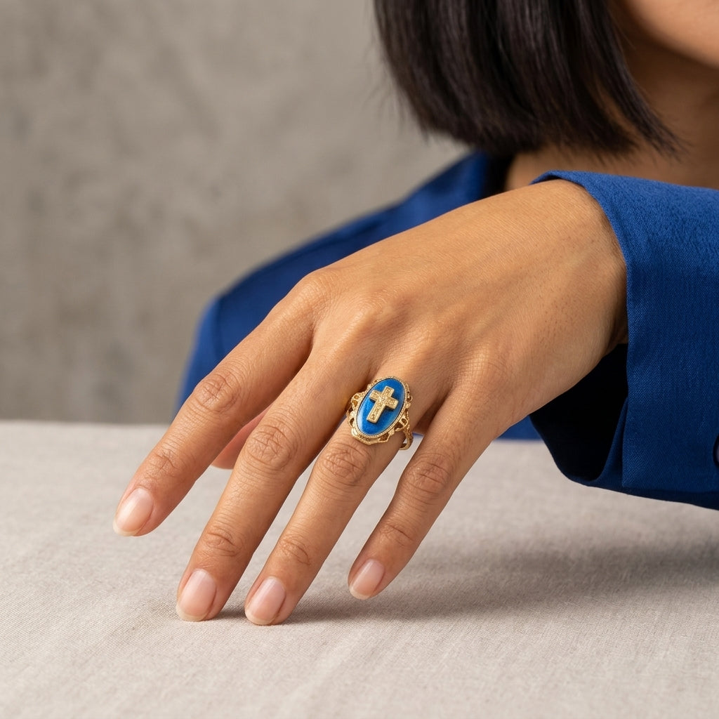 Hand wearing a gold cross ring with a blue stone on a neutral background