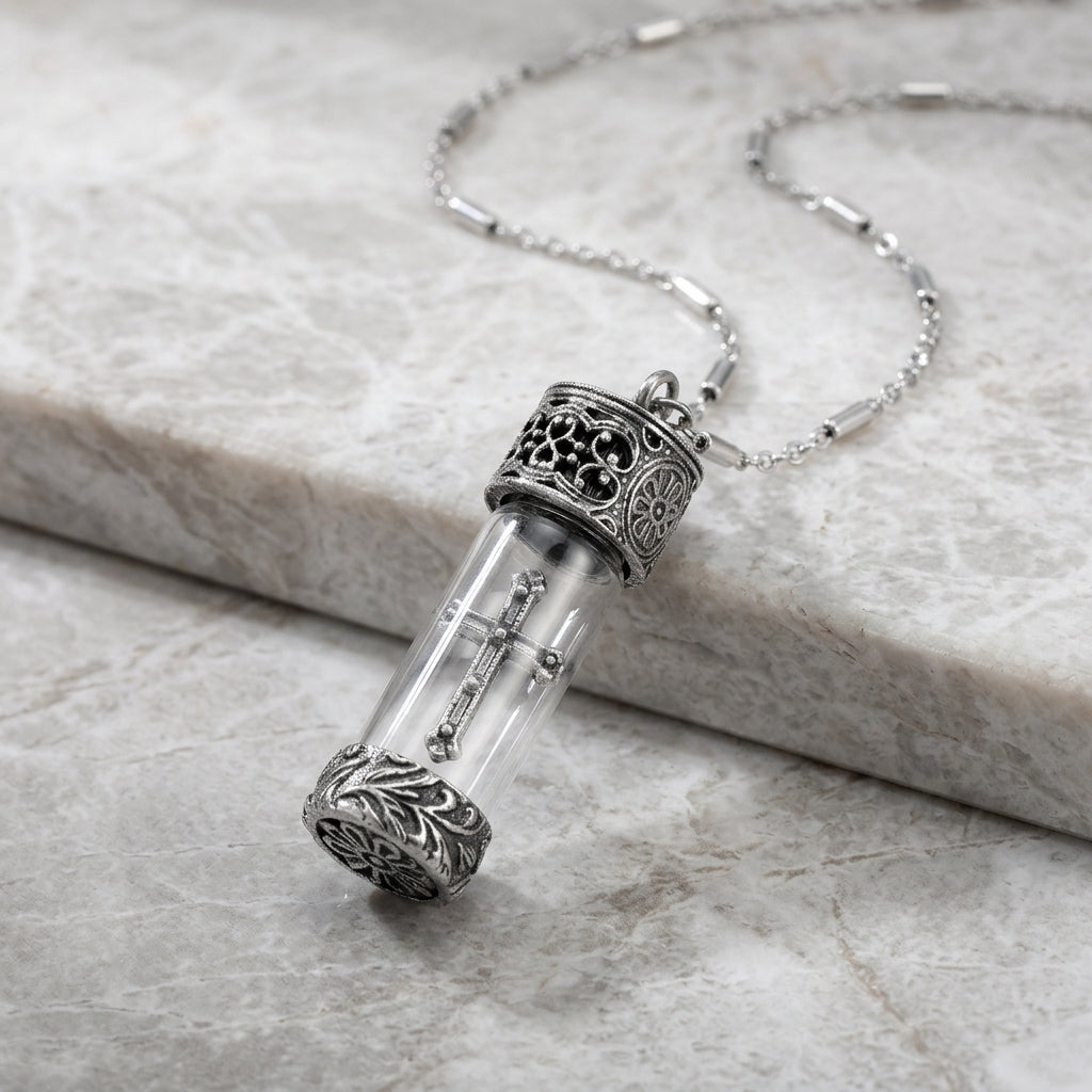 Silver necklace with a clear glass vial pendant and cross design on a marble surface