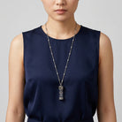 Person wearing a long vial pendant necklace with a blue dress on a plain background