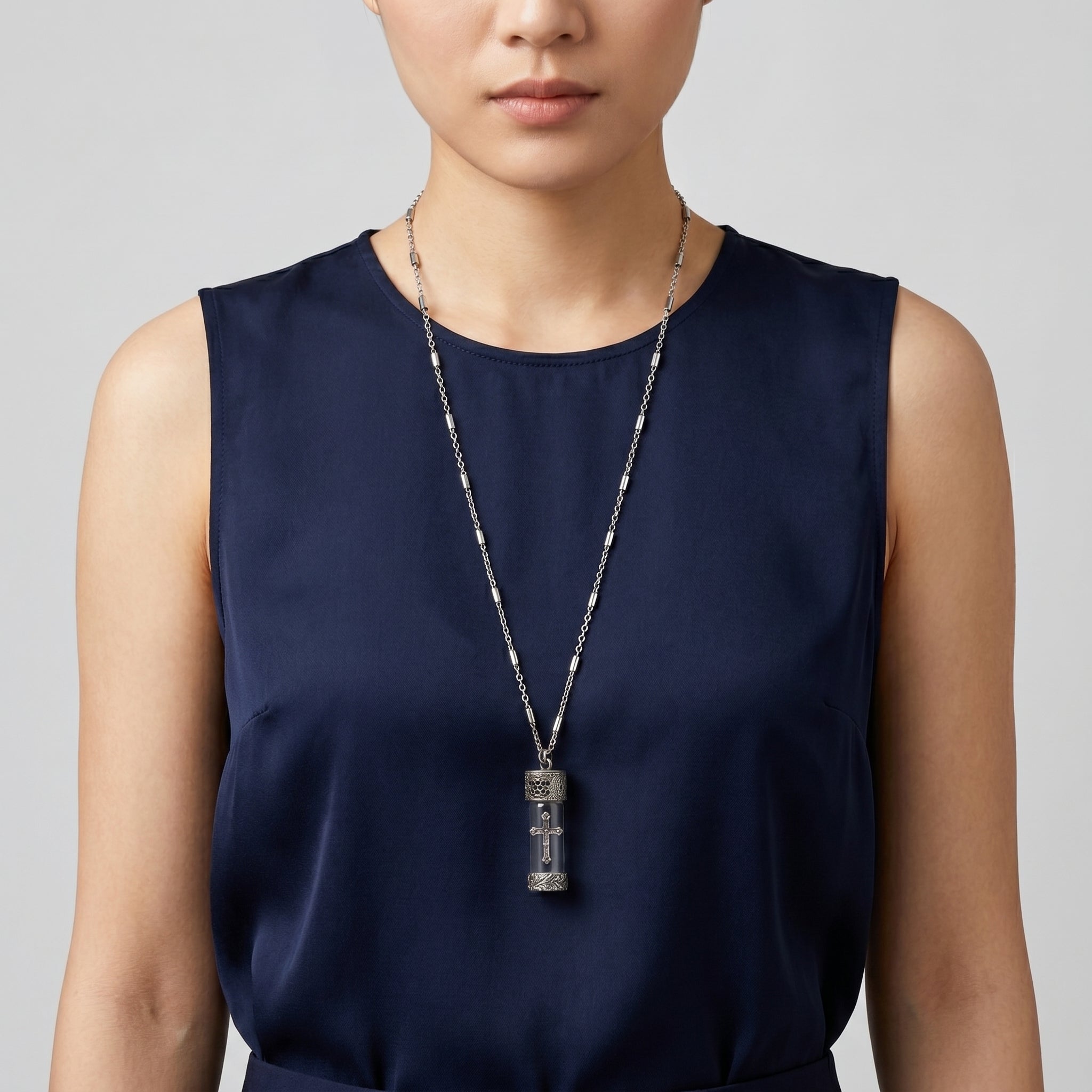 Person wearing a long vial pendant necklace with a blue dress on a plain background