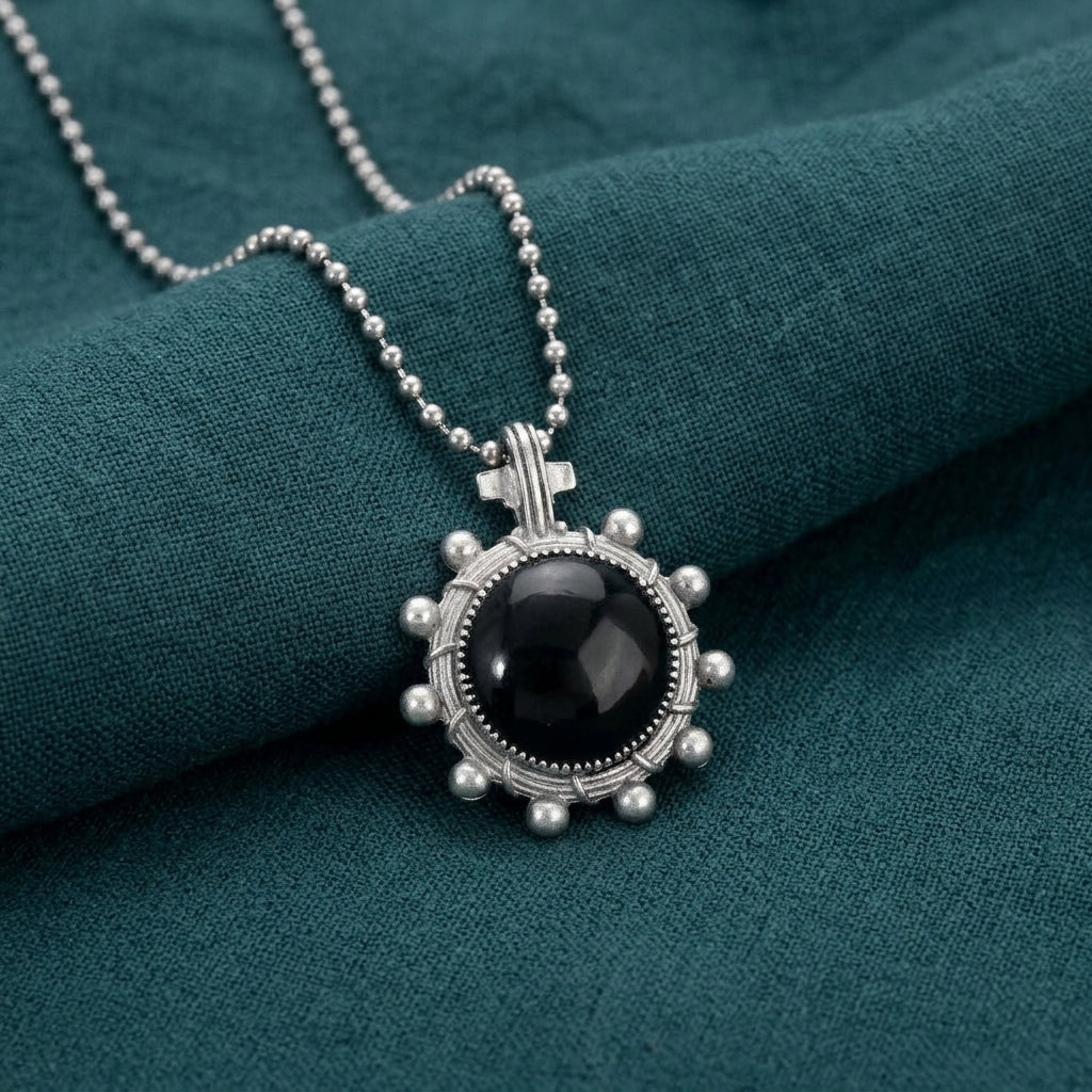 Silver necklace with a black pendant on a teal fabric background