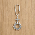 Silver keychain with a rosary cross design on a wooden surface