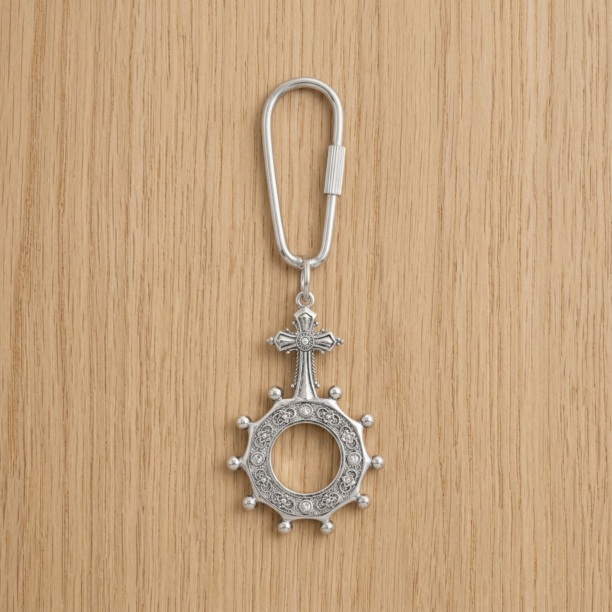 Silver keychain with a rosary cross design on a wooden surface