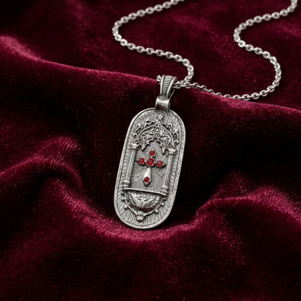 Silver pendant with red crystals and a cross design on a chain, placed on a red velvet surface