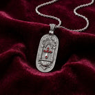 Silver pendant with red crystals and a cross design on a chain, placed on a red velvet surface