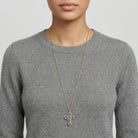 Person wearing a long necklace with a blue crystal cross pendant on a plain background