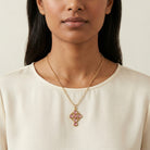 Woman wearing a gold necklace with a pink crystal and cross pendant against a neutral background