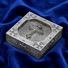 Decorative metal rosary box with intricate designs on a blue fabric background