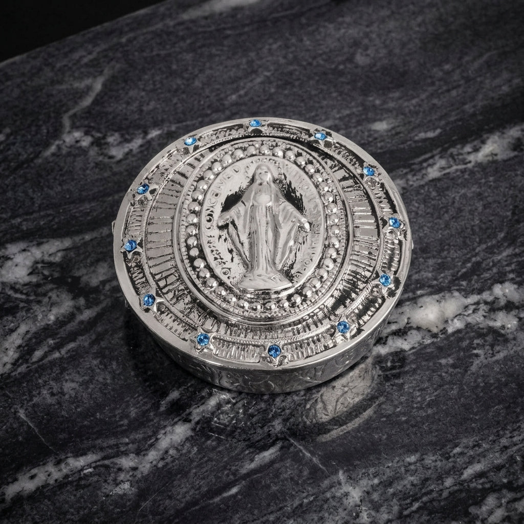 Silver round decorative pillbox with religious design on a marble surface