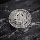 Silver round decorative pillbox with religious design on a marble surface