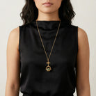 Woman wearing a black sleeveless top with a gold tone necklace featuring a cross-design spinner pendant with three different types of gemstones