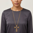 Person wearing a gold cross necklace with a blue enamel center on a plain background