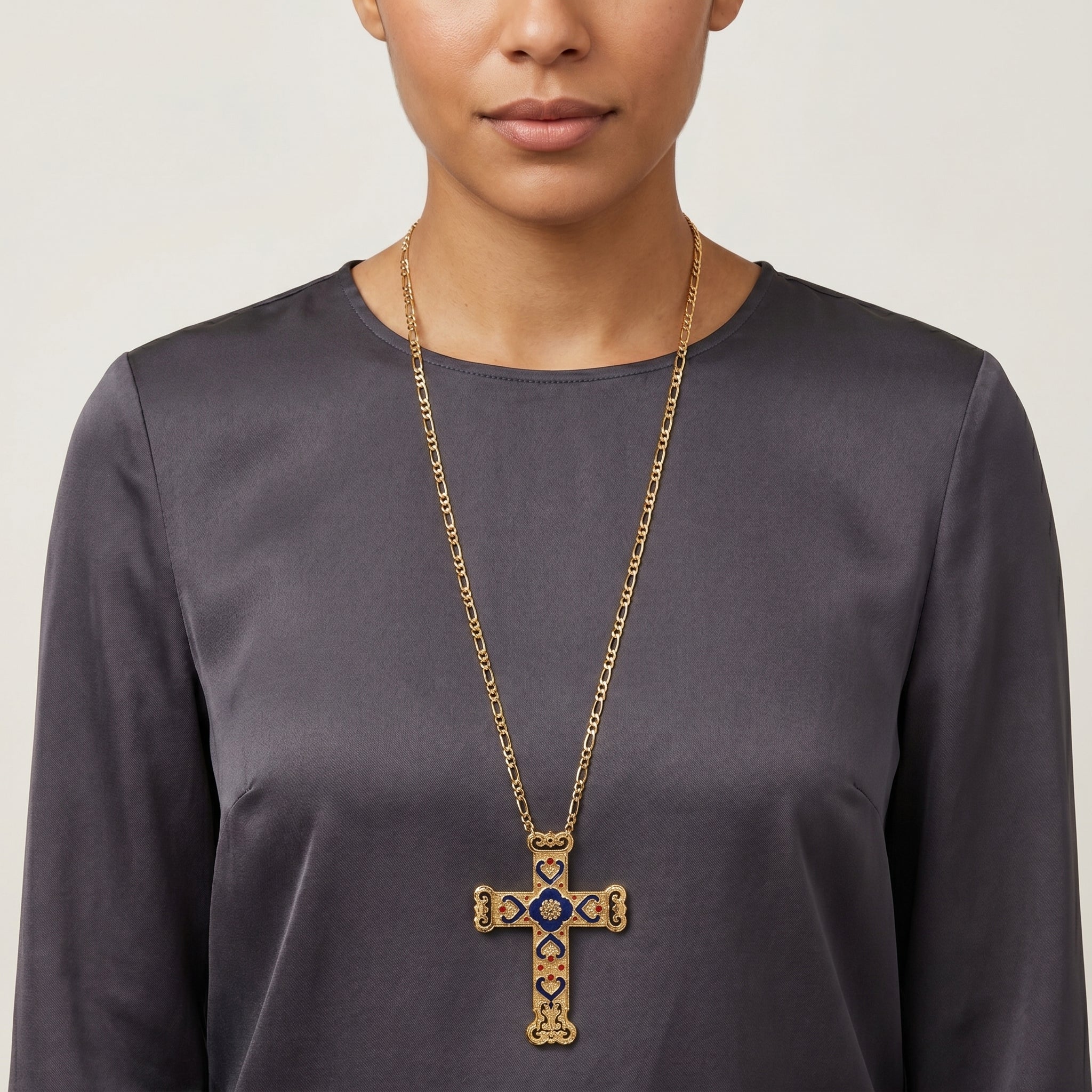 Person wearing a gold cross necklace with a blue enamel center on a plain background