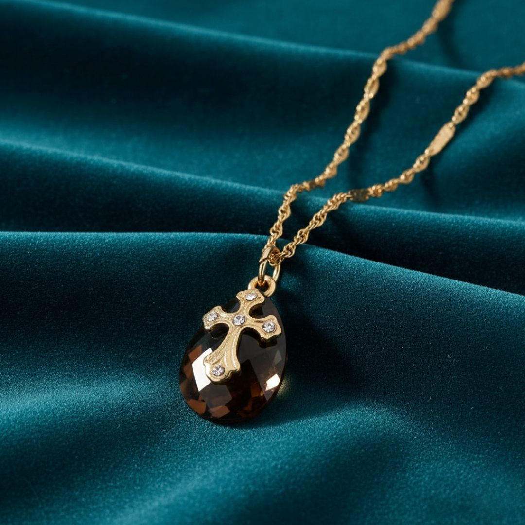 Gold necklace with a dark cross pendant with a crystal on a teal fabric background