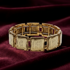 Gold bracelet with engraved Ten Commandments on a red fabric background.