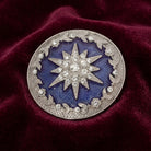 Decorative brooch with Star of Bethlehem design on a blue background, placed on a red fabric surface.