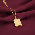 Gold necklace with a Bible-shaped pendant featuring a cross on a maroon fabric background