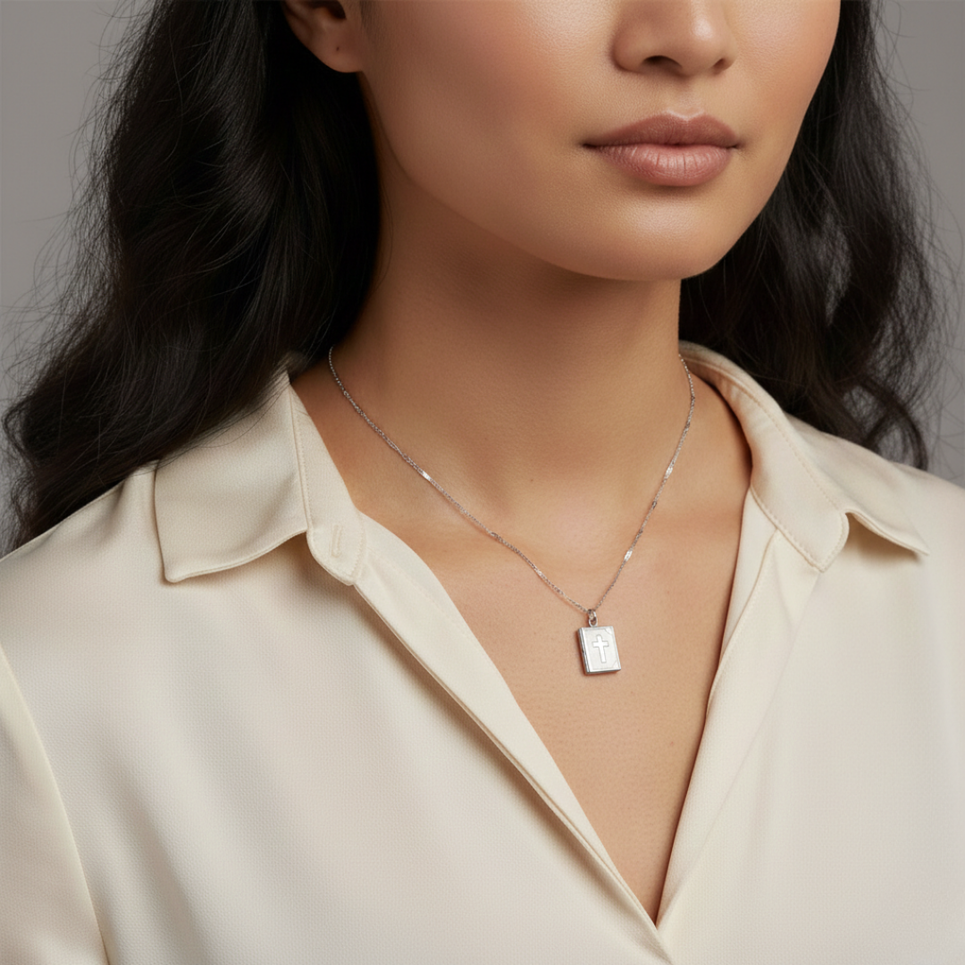Close-up of a person wearing a silver necklace with a rectangular Bible pendant against a neutral background