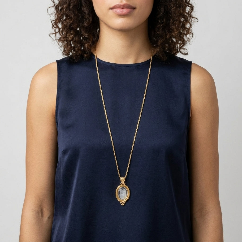 Woman wearing a long gold necklace with an oval intaglio religious pendant on a plain background