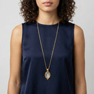 Woman wearing a long gold necklace with an oval intaglio religious pendant on a plain background