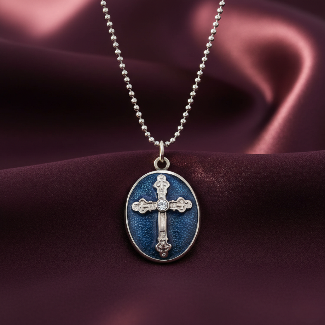 Blue oval pendant with cross design on a silver chain against a purple fabric background