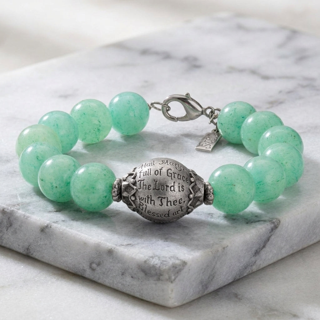 Green beaded bracelet with a silver tone engraved Hail Mary prayer on a marble surface