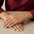 Gold bracelet with religious charms on a hand against a neutral background